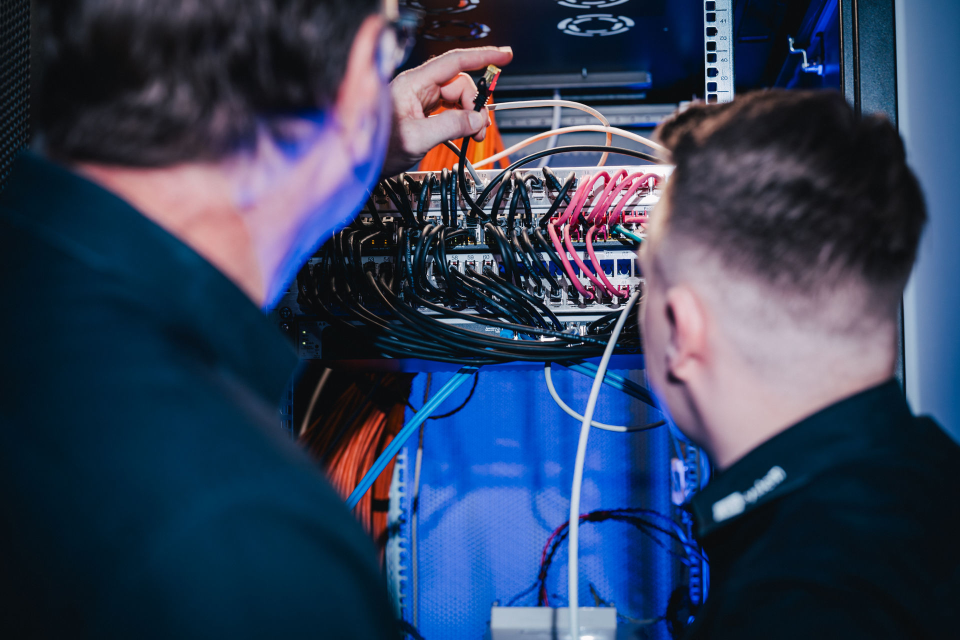 Zwei Techniker von hcsystem arbeiten an Patchfeld und Switch in einem Netzwerkschrank.