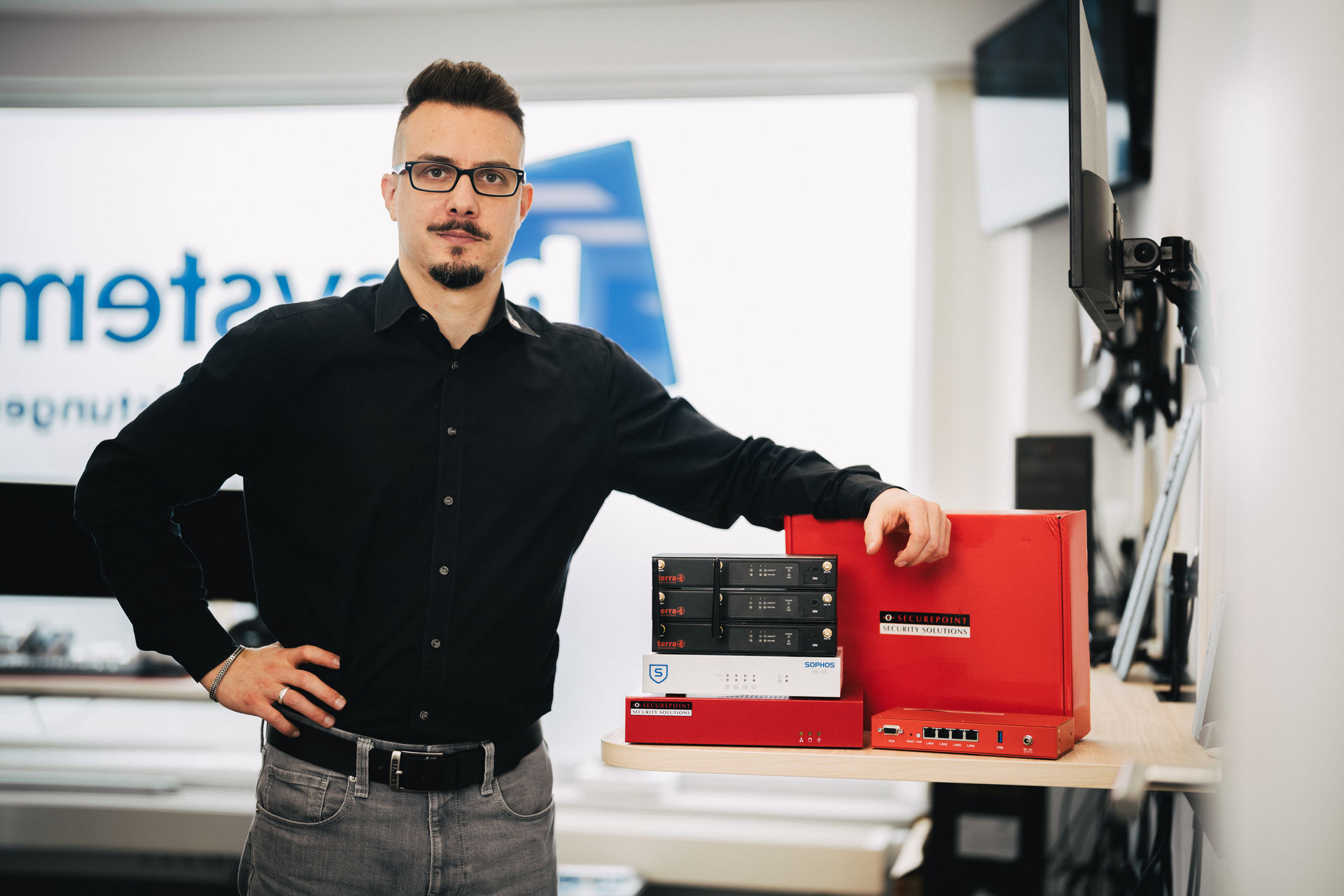 Dominic Höfer von hcsystem neben mehreren gestapelten Firewall-Geräten.